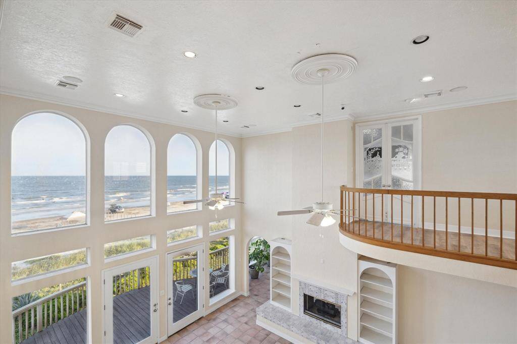 Bright, coastal-style interior with arched windows overlooking the beach, featuring a fireplace, balcony, and high ceilings.