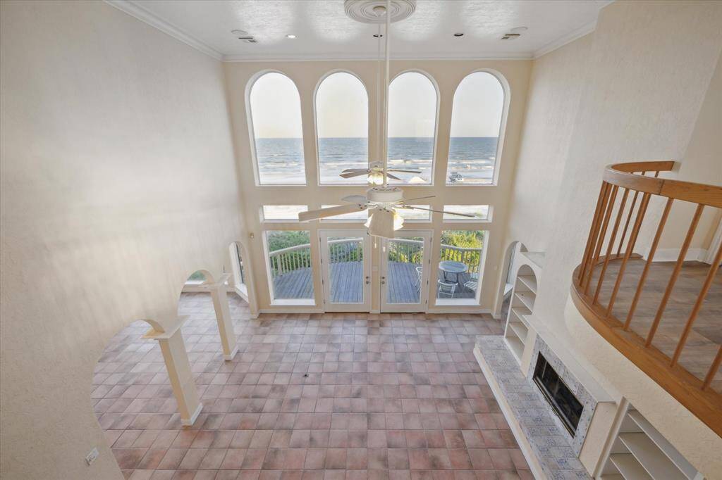 Bright, airy room with arched windows overlooking the ocean, tiled floor, wooden railing, and a ceiling fan.