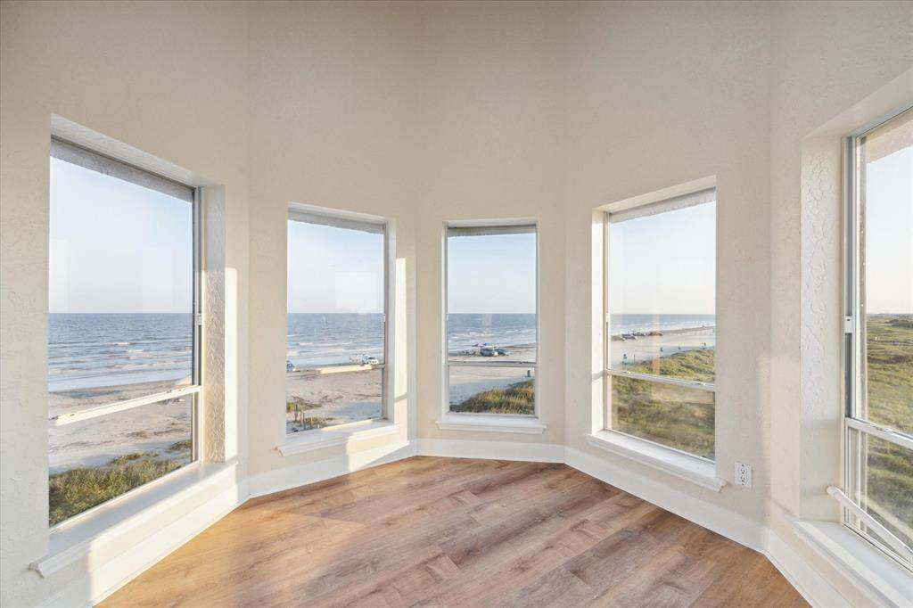 Sitting or exercise room with large windows offering a panoramic view of a beach, dunes, and a distant parking area under a clear sky.