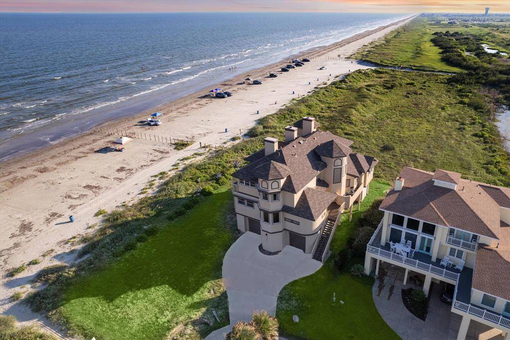 This is a luxurious beachfront property with direct access to the beach, showcasing a large, elegant home with multiple stories and a well-manicured lawn, set in a serene coastal environment.