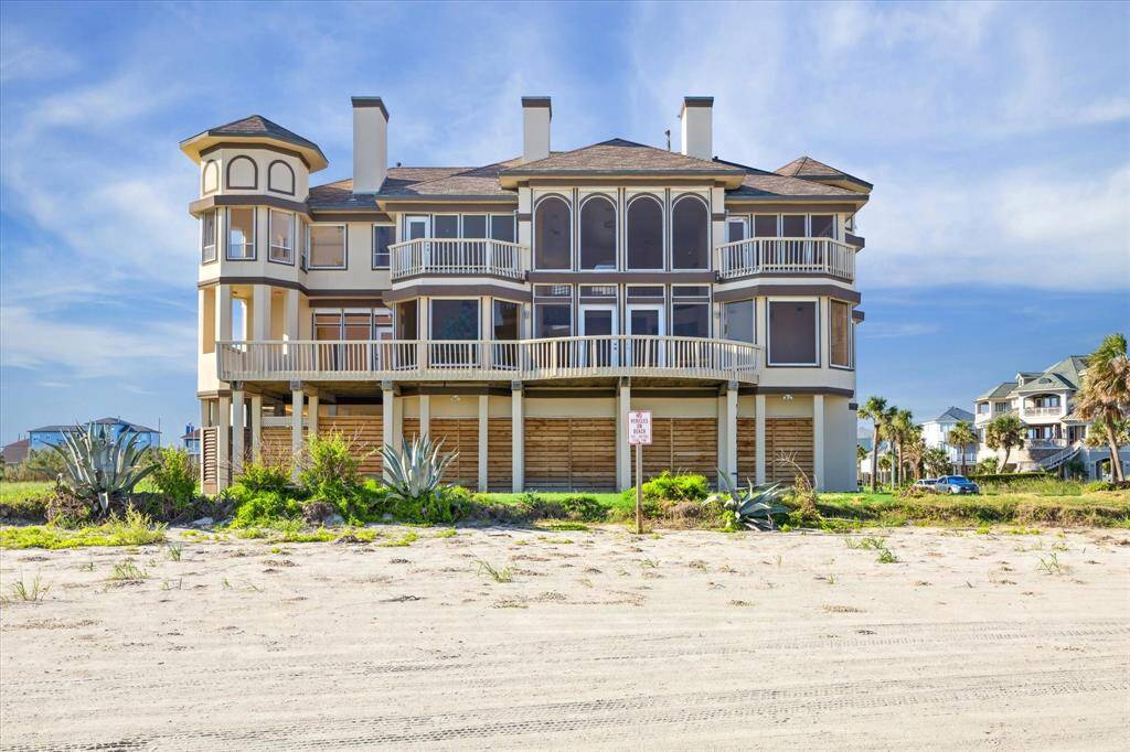 A large multi-story beachfront house with balconies, overlooking Galveston state park and other homes, with a vibrant sky.