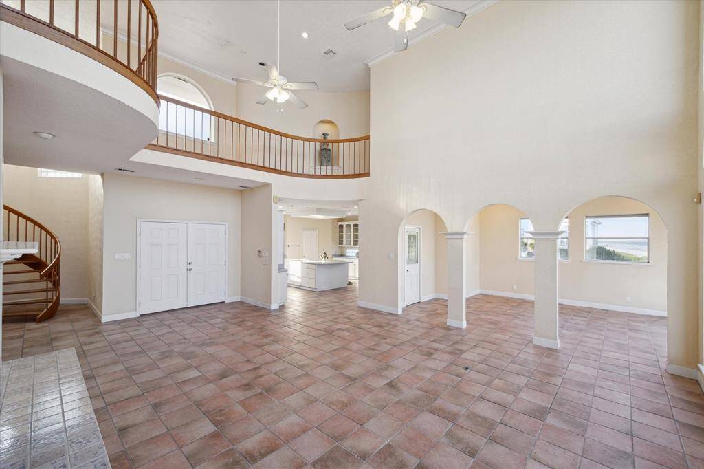 Spacious with high ceilings, tile flooring, curved staircase, arched openings, and abundant natural light from windows.