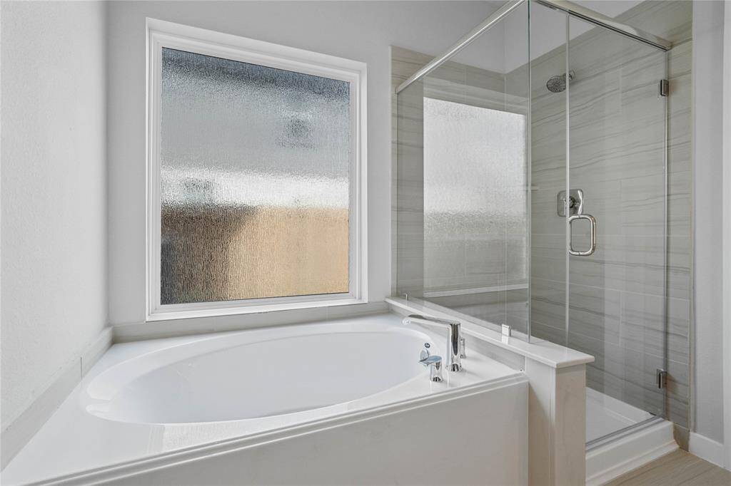 Additional view of the primary bathroom featuring a walk-in shower with tile surround and separate garden tub for soaking after a long day with custom tile detailing.