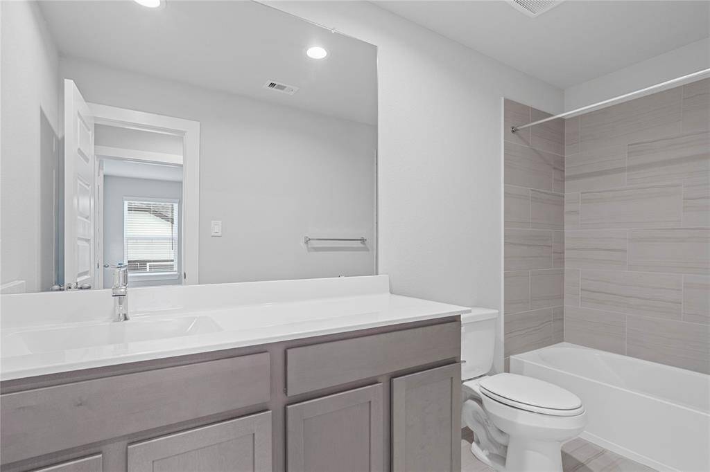 Secondary bath features tile flooring, bath/shower combo with tile surround, stained cabinets, beautiful light countertops, mirror, sleek fixtures and modern finishes.