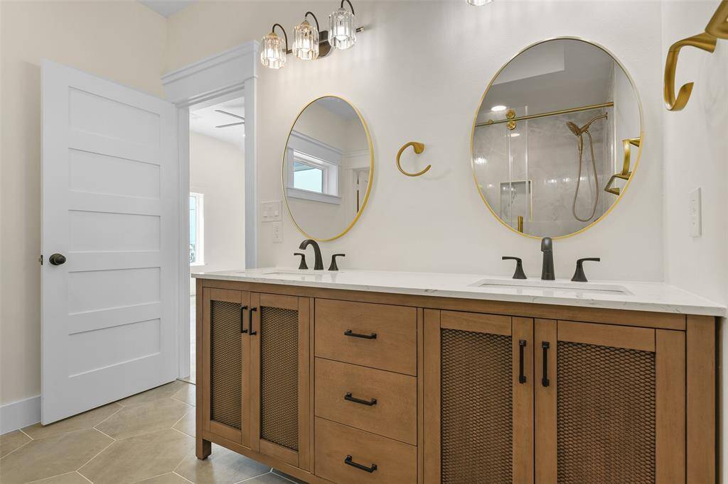The primary ensuite has a modern and coastal vibe. It features a double vanity with stylish gold-trimmed mirrors, elegant lighting fixtures, and a neutral color scheme.