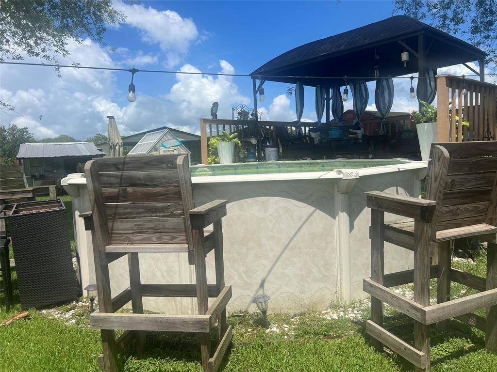 This outdoor space includes a above-ground pool and a covered bar or seating area, ideal for entertainment and relaxation. Rustic wooden chairs and decor add to the cozy backyard ambiance.