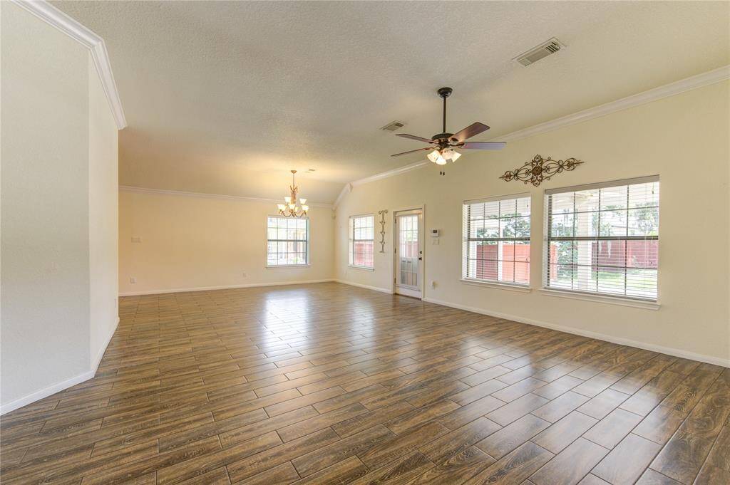 The large combo living/dining features wood-look tile flooring, large windows with a view of the yard, and a ceiling fan. The neutral wall colors provide a versatile backdrop for various decorating styles.