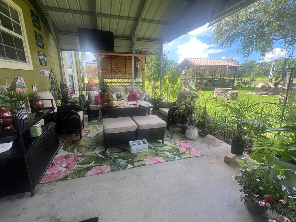 A spacious, covered outdoor back door patio area with comfortable seating, vibrant plant life, and a view of a well-maintained garden with a gazebo, offering an ideal space for relaxation and entertaining.