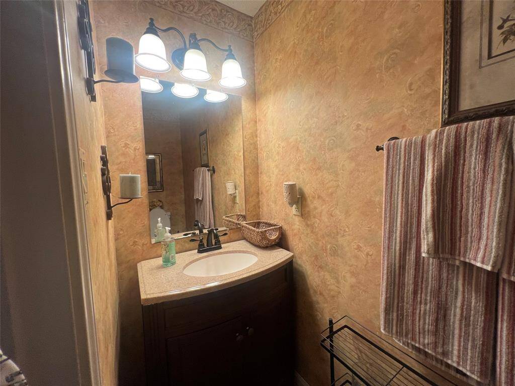 This is a guest bathroom featuring a single vanity with an undermount sink and ample lighting, accented by a decorative mirror and warm, patterned wall treatment.