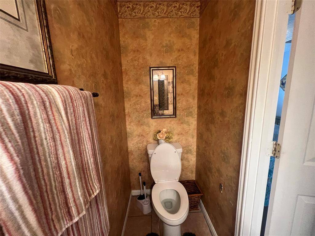 This is another view of the guest bathroom featuring a toilet, adorned with a wall-mounted mirror and decorative finishes. The space has a textured wall treatment and crown molding, creating a classic aesthetic.