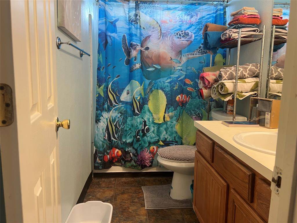 You're looking at a vibrant marine-themed upstairs bathroom featuring a colorful underwater scene shower curtain, a wood-finished vanity with a countertop sink, and a well-organized towel rack with plenty of linens. The space offers a playful touch to a functional bathroom setting.