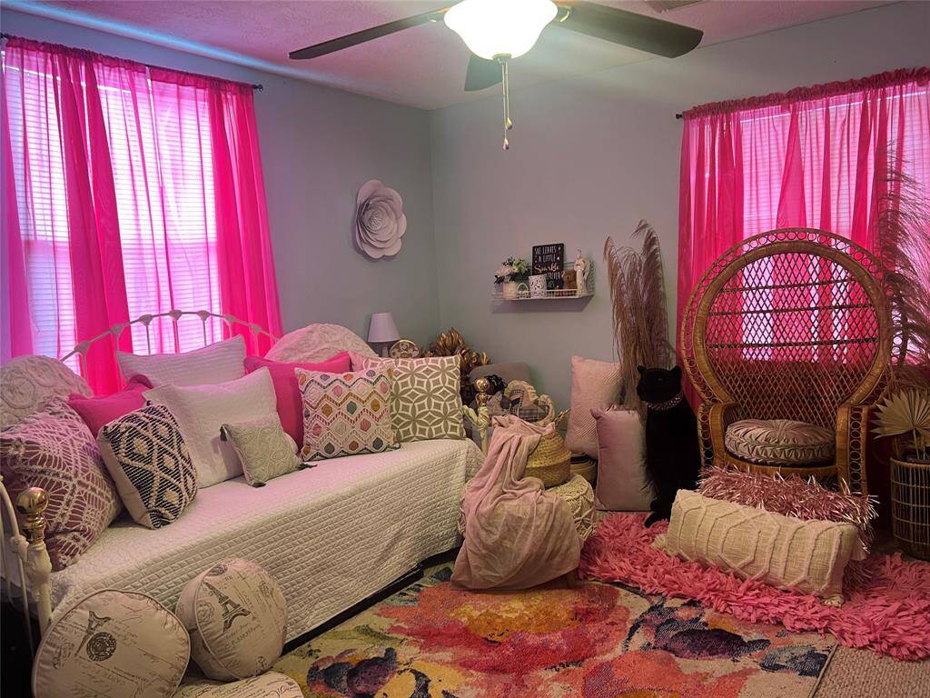 This is a cozy guest bedroom with vibrant pink curtains, eclectic decor, and a unique peacock chair, creating a playful and personalized space.