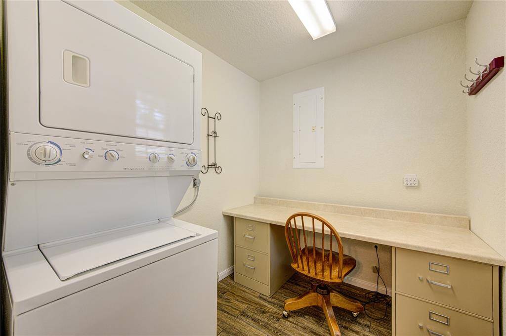 Great laundry room featuring a stacked washer and dryer unit, ample counter space for folding clothes, built-in cabinetry for storage, and a small desk area. It is well-lit with a modern light fixture.