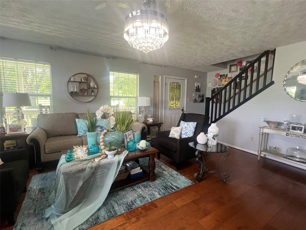 This is a different angel of the living room with hardwood floors, featuring a mix of modern and classic elements. The room includes comfortable seating, decorative accents, and an elegant chandelier, with ample natural light from the large windows and a staircase leading to the upper level.
