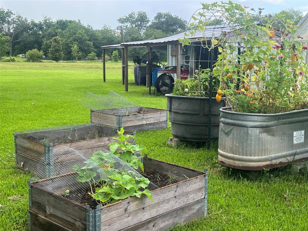 More lush, green backyard with raised garden beds and larger metal containers used for gardening. There's a rustic outdoor shed, and the property appears to have ample space for outdoor activities and gardening.