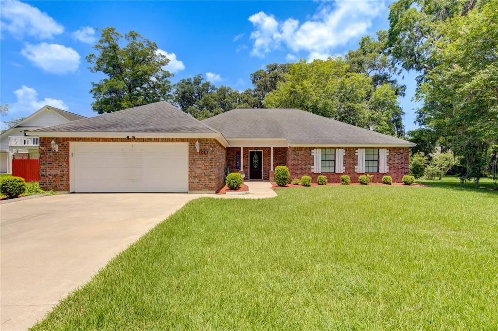 This is a single-story brick home featuring a two-car garage, well-maintained lawn, and mature trees providing shade and curb appeal.