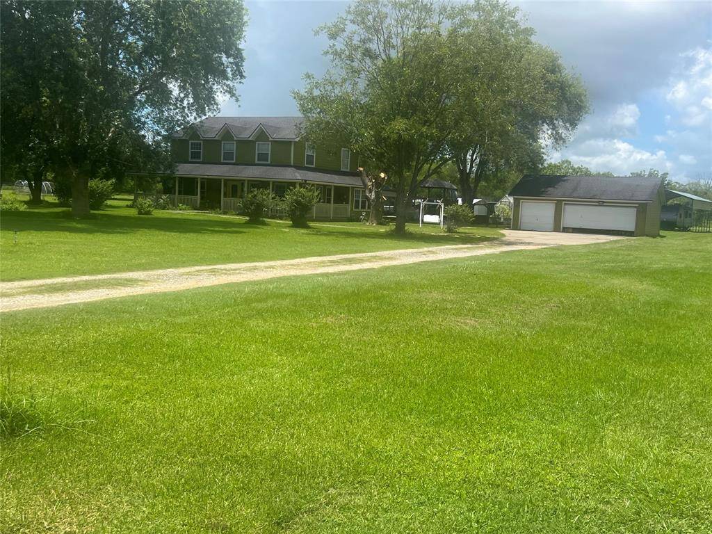 You're looking at a two-story house with a large front yard, mature trees, a covered porch, and a separate two-car garage. The setting appears peaceful with ample green space.