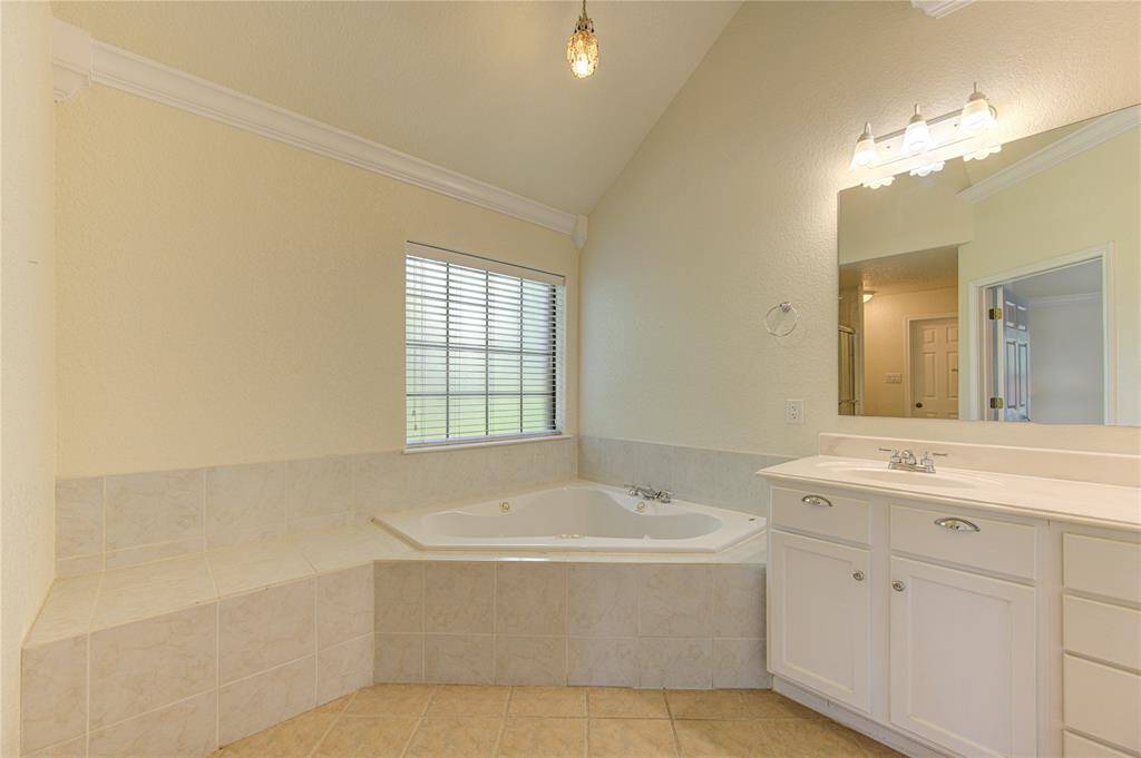 Spacious bathroom featuring a large corner bathtub under a window, dual vanity with ample storage, and tiled flooring.