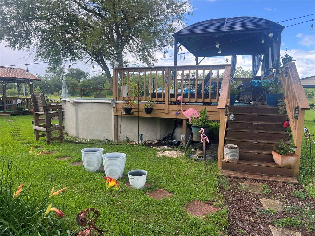 This elevated wooden deck that includes a covered pergola area. The deck overlooks a well-maintained lawn adorned with flowering plants and decorative elements, creating a welcoming outdoor living space ideal for relaxation and entertainment. Jump into this never used pool and relax in the shade  of this gazebo on a hot sunny day!