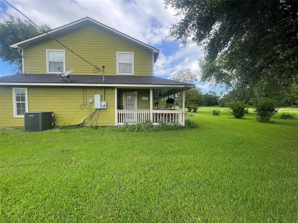 This is a two-story home with a green exterior and white trim, featuring a covered front porch and a spacious lawn. It includes a satellite dish and an AC unit on the side. Showing more spacious greenery throughout the property.