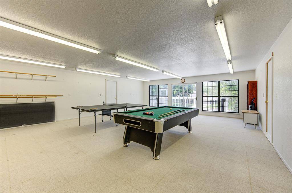This is a spacious, multi-purpose room featuring ample lighting, a billiards table, and a table tennis setup, with large windows providing natural light and a view to the outside. The room also includes built-in wall shelving and easy-to-clean flooring, perfect for entertainment or a hobby area.