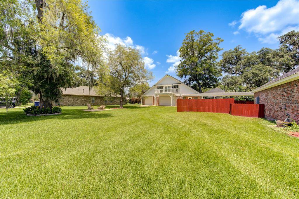 Spacious backyard with a well-maintained lawn, mature trees providing shade A red wooden fence adds privacy.