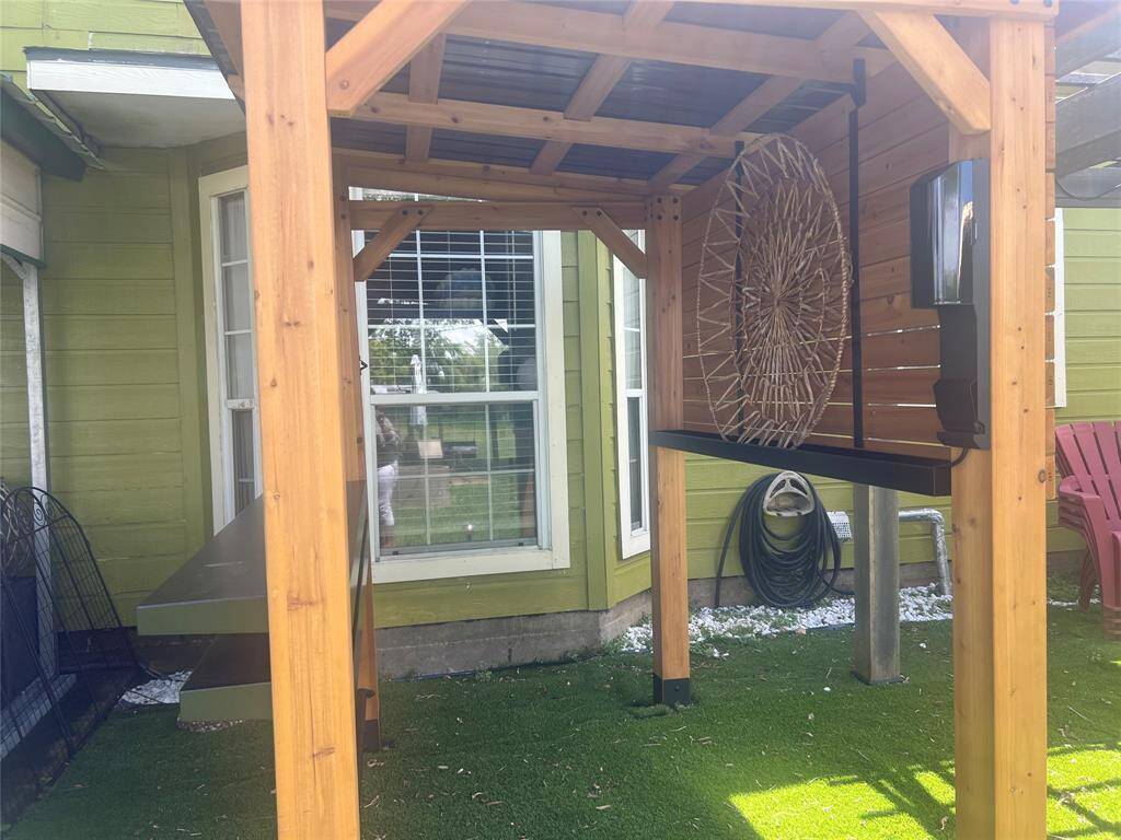 This is an outdoor area featuring a sturdy wooden pergola with a built-in bar counter, ideal for entertaining. The space is enhanced with green exterior walls, creating a cozy, welcoming atmosphere.