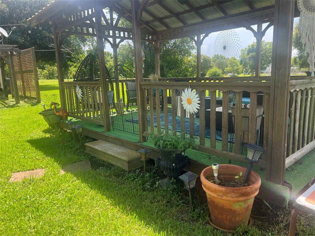 The backyard also showcases a charming a wooden gazebo, which includes a bench and decorative elements such as hanging planters and a large daisy ornament. The space is accessorized with garden lights, potted plants, and a trellis, creating a cozy outdoor retreat.