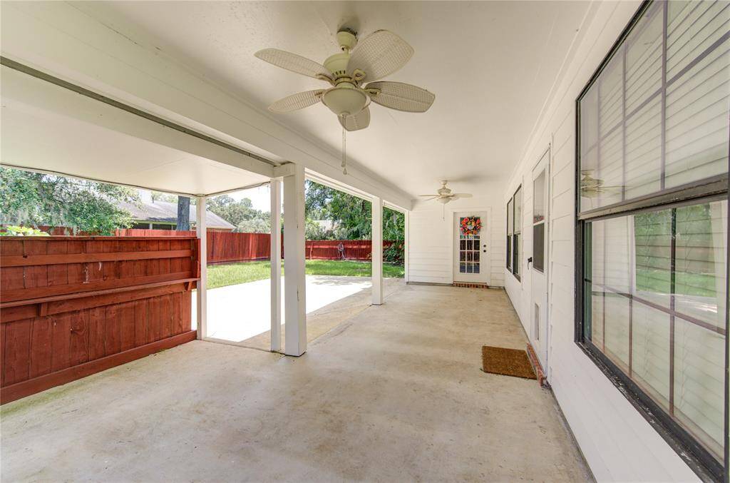 Large covered patio area with a ceiling fan, overlooking a fenced backyard, perfect for outdoor relaxation and entertainment.
