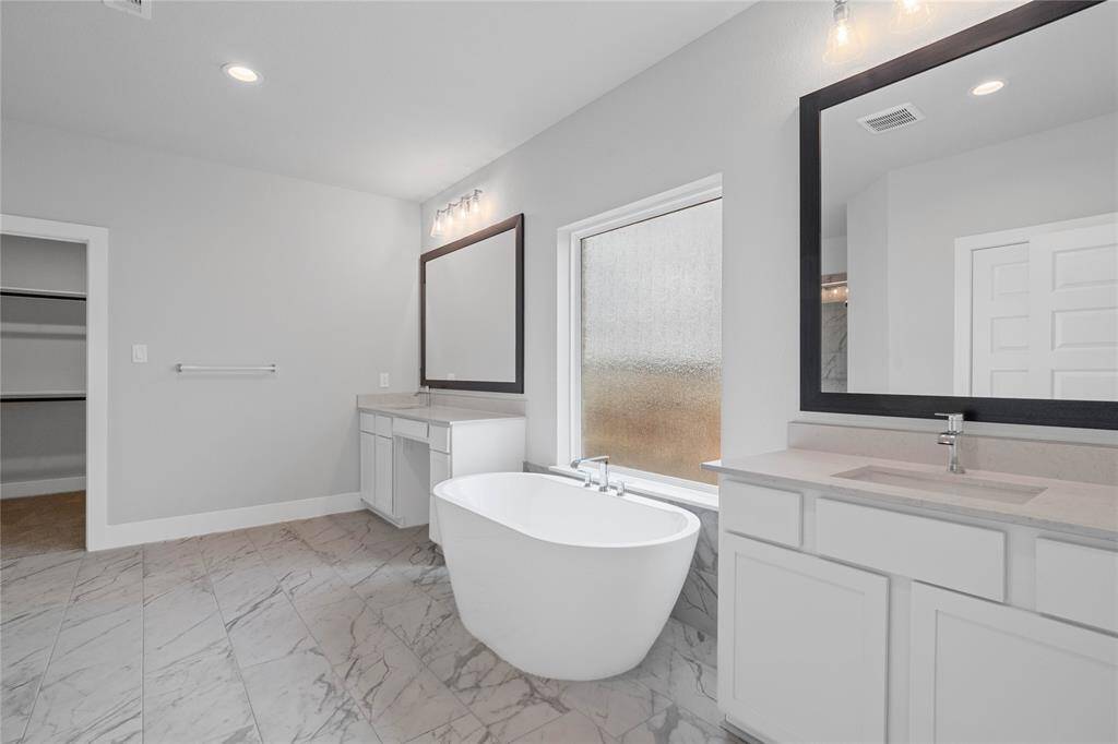 This primary bathroom is definitely move-in ready! Featuring a separate garden tub for soaking after a long day with custom tile detailing, stained cabinets with countertops, spacious walk-in closet with shelving, high ceilings, custom paint, framed mirrors, sleek and dark modern finishes.