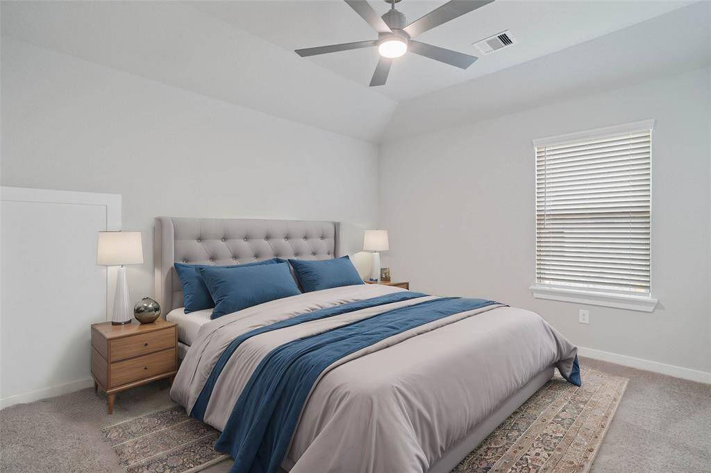 Secondary bedroom features plush carpet, custom paint, ceiling fan with lighting and a large window with privacy blinds.