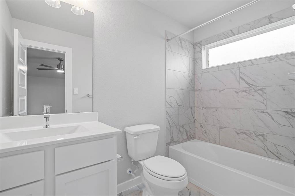 Secondary bath features tile flooring, bath/shower combo with tile surround, white stained wood cabinets, beautiful light countertops, mirror, dark, sleek fixtures and modern finishes.