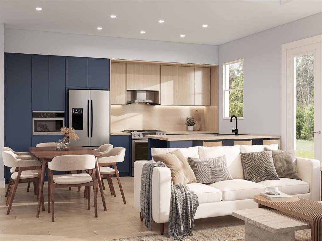 Plans convey with the purchase. Modern open-plan living space with a fully equipped kitchen featuring blue cabinetry and wooden accents, a cozy dining area. Natural light streams in through a window and glass door leading to outdoor greenery.