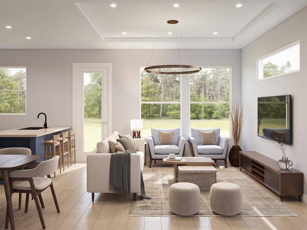 This is a spacious and modern open-plan living space featuring a lounge area, a dining area, and a kitchen with a breakfast bar. Large windows allow for plenty of natural light and views of the greenery outside. The interior design includes neutral tones creating a warm and inviting atmosphere.