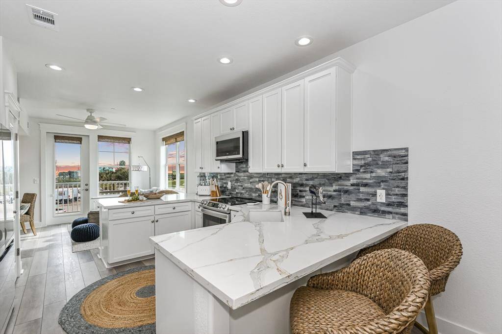 Admire the beauty of this stunning kitchen, boasting state-of-the-art Samsung Bespoke white glass appliances, complemented by a meticulously crafted custom tile backsplash. With its soaring ceilings, elegant recessed lighting, and upgraded floors, every corner emanates sophistication. Plus, indulge in the luxury of not one, but two inviting breakfast bars, offering a serene view of the bay.