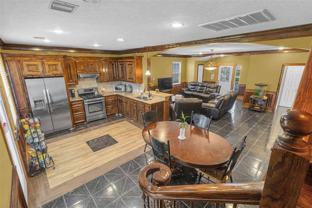 This is a spacious open-concept living area with a well-equipped kitchen featuring stainless steel appliances and wooden cabinetry, a dining area, and a comfortable living room. The space is complemented by tile flooring and wooden accents.
