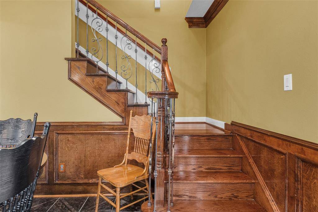 This is a warm and inviting staircase with elegant wood paneling and wrought-iron railings, complemented by a rich wooden staircase. The space features a yellow wall color and tile flooring at the base, adding to the home's classic charm.