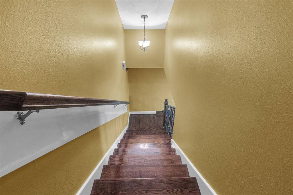 This is a stairway with warm yellow walls, dark wood floors, and a classic wooden handrail with white accents. A traditional light fixture illuminates the space.