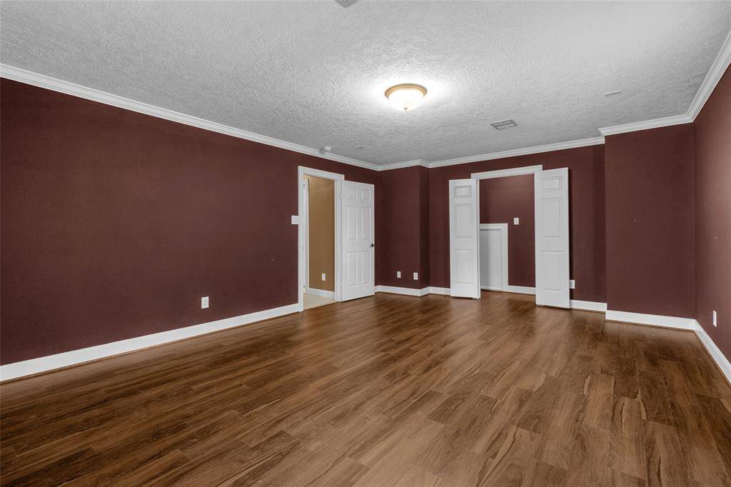 This is a spacious room featuring rich burgundy walls with white trim, hardwood floors, textured ceiling, and a large window providing natural light.