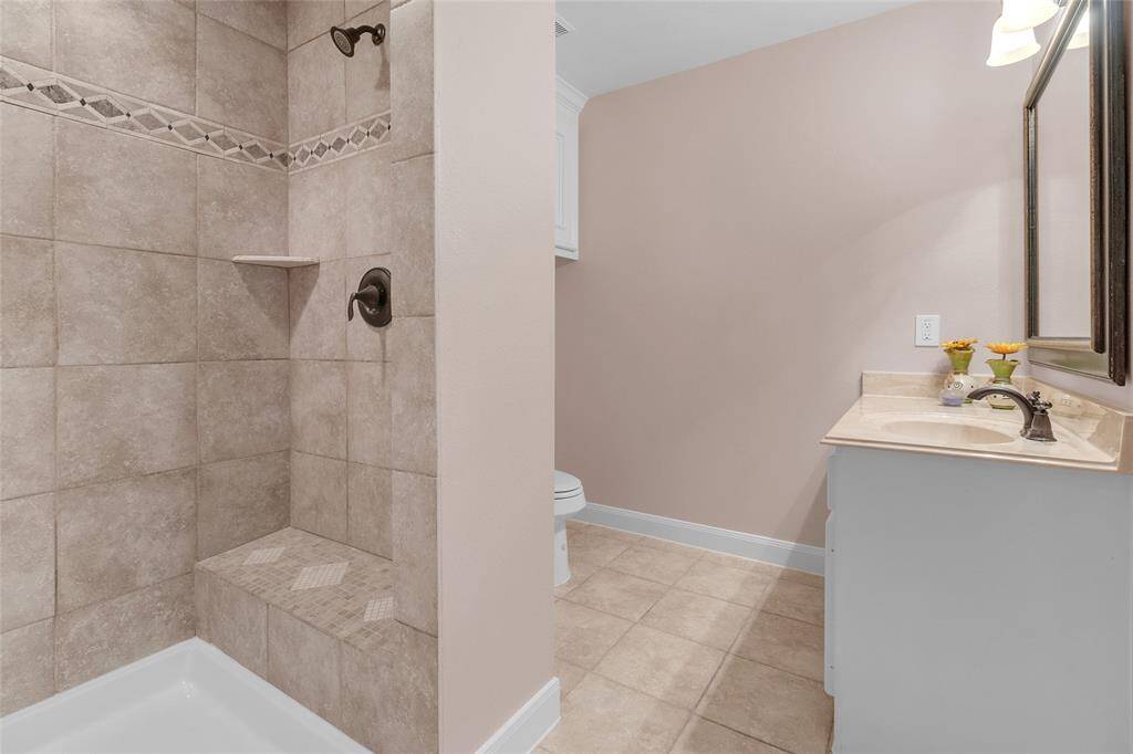 Modern bathroom with a corner soaking tub, a separate shower stall, and a toilet. Neutral tiles with decorative accents line the walls, and there's built-in cabinetry for storage.