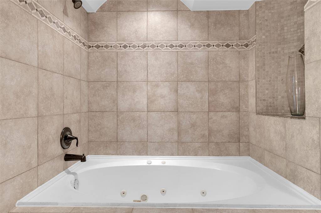 Indulge in luxury with this sleek bathroom, featuring a spacious corner tub perfect for relaxation, an elegant separate shower enclosure, and stylish built-in storage—all complemented by tasteful neutral tiling with artful accents.