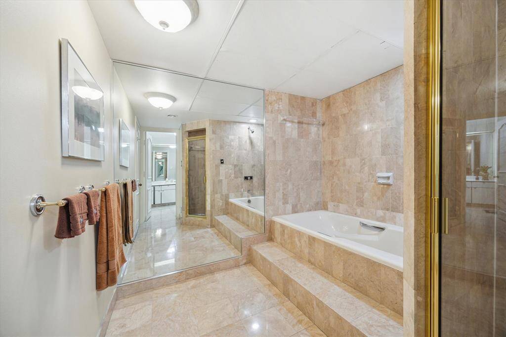 Ensuite bath off primary bedroom is divided into two spaces.  Tub with separate shower shown here. Room at the end for vanity.  Marble /travertine adorns walls and floors.