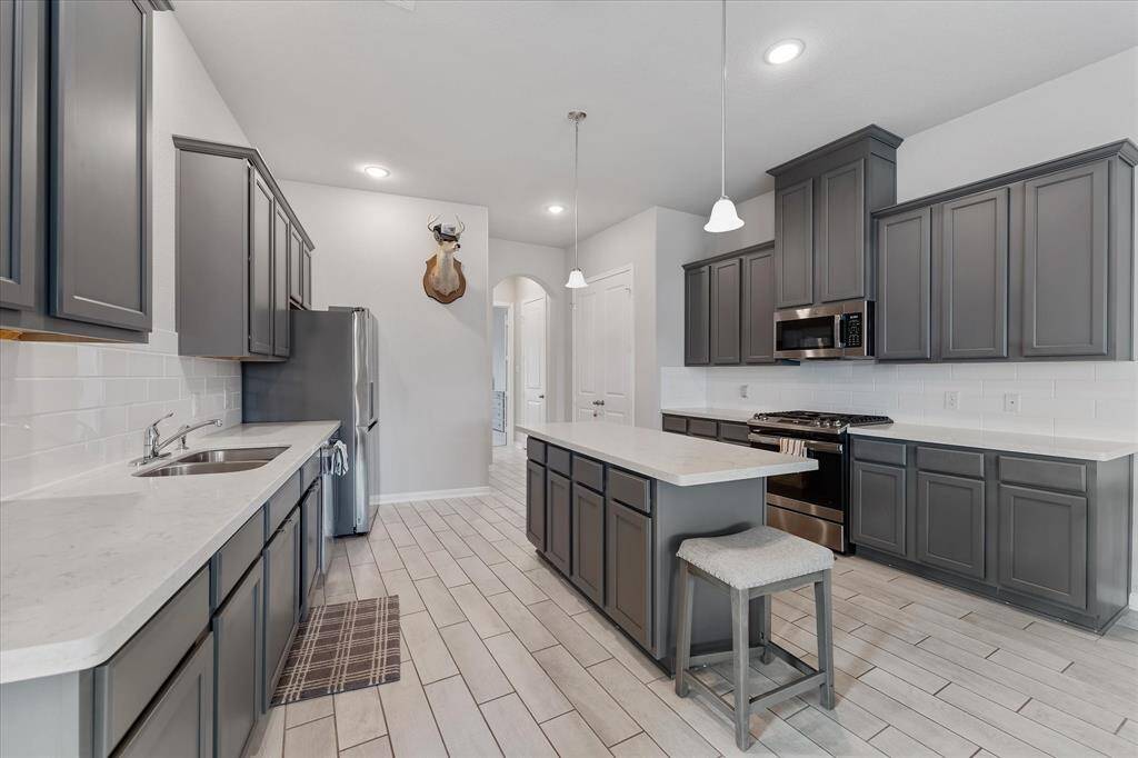 The modern kitchen features a center island, gas cooking, stylish gray cabinetry, and pristine white countertops.