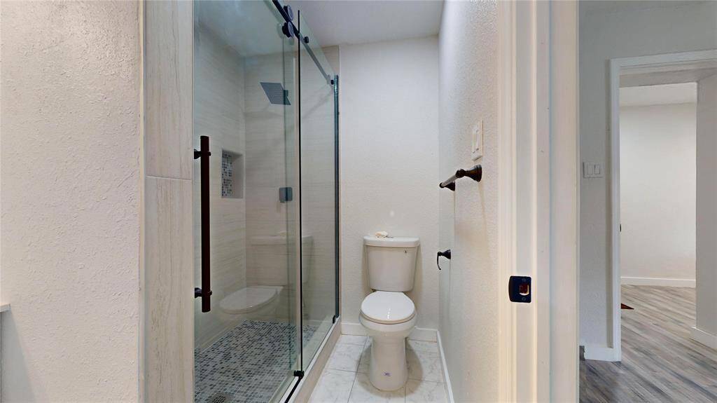 This is a modern bathroom featuring a walk-in shower with a glass door, sleek fixtures, and a toilet.