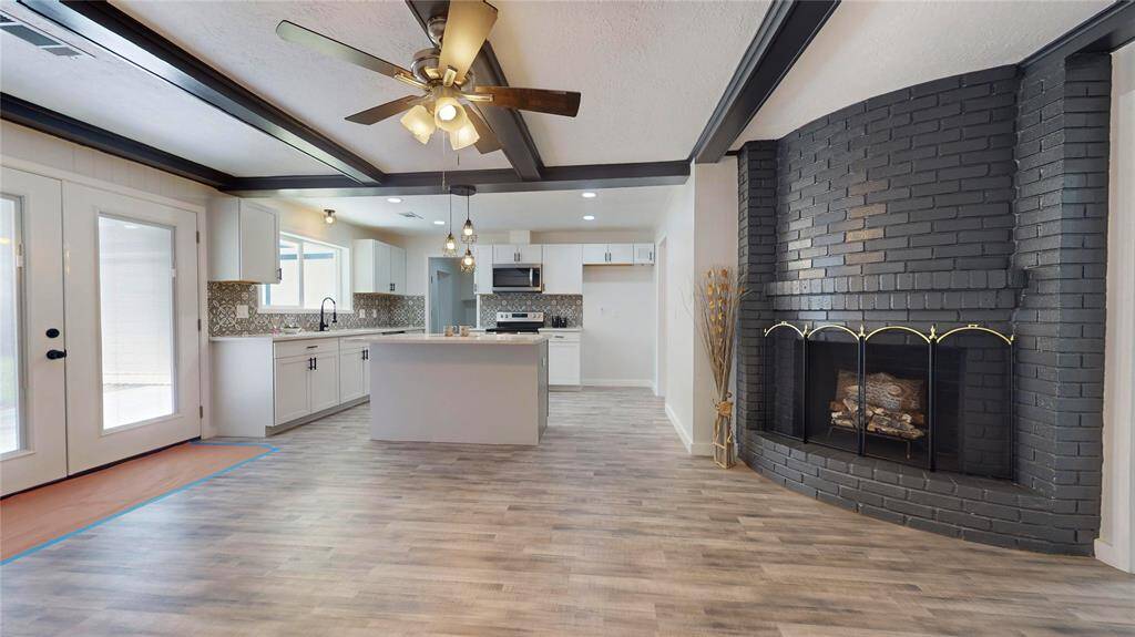 Spacious and modern open-concept living space having a cozy fireplace with a dark painted brick surround.