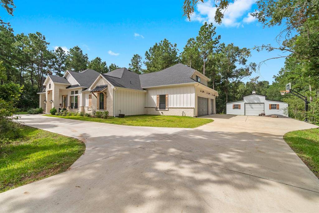 This is a spacious single-story home with a large driveway, attached garage, and a separate outbuilding, surrounded by mature trees offering privacy and a serene setting.