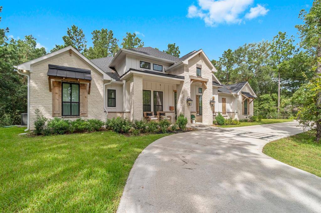 This is a modern single-story home with an elegant brick facade, featuring a large driveway and surrounded by lush greenery for privacy.