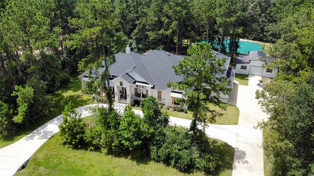 This is an aerial view of a spacious single-family home with a pond, surrounded by lush greenery, featuring a sizable driveway and an attached garage.