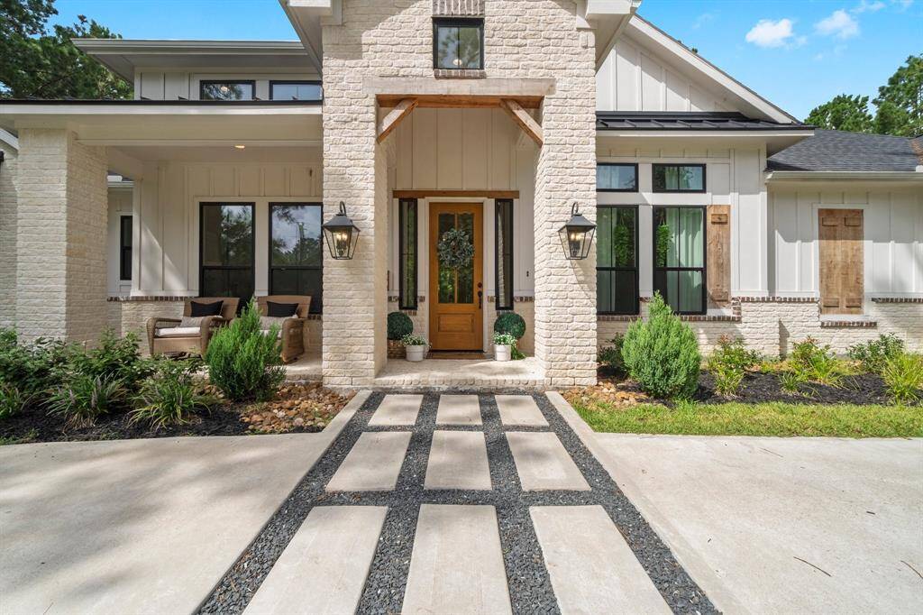 This is a modern home with a striking stone facade and a welcoming entrance that features a unique pathway leading to a wooden front door. The property has a well-manicured front yard with lush landscaping and a cozy covered porch area with seating. Large windows and warm exterior lighting add to the home's inviting ambiance.