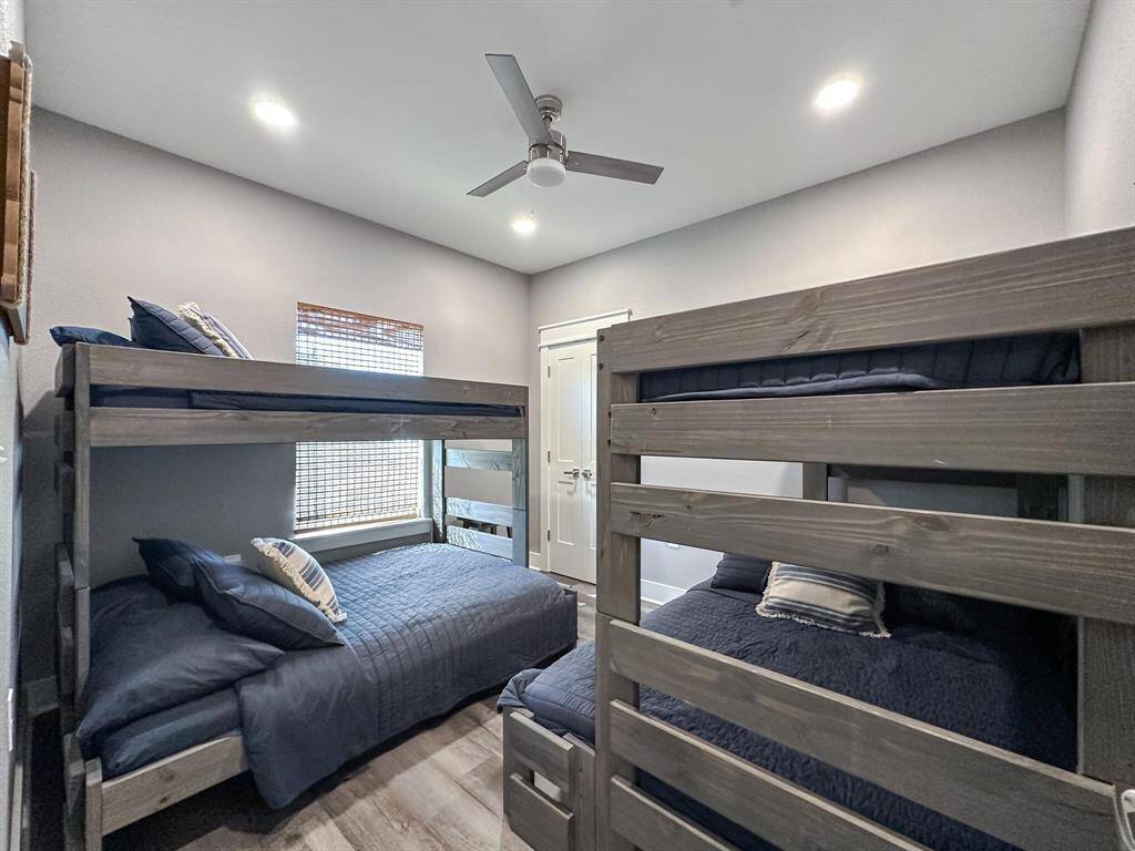 This is a neatly presented bedroom featuring a set of wooden bunk beds with navy blue bedding, a ceiling fan, and a window with blinds providing natural light.